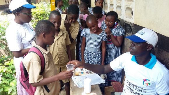 A group of villagers wait to receive their medication from the local community drug distributor, who hands them a cup containing the tablets.