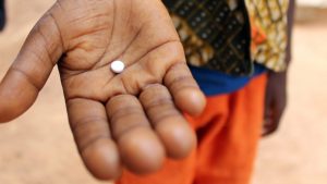 A close up of a person's hand holding a medication tablet.