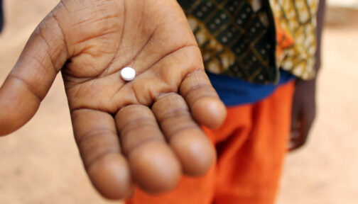 A close up of a person's hand holding a medication tablet.