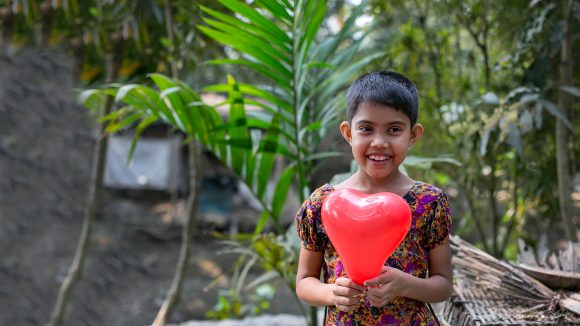 Muslima holds up a balloon to the camera and smiles broadly.