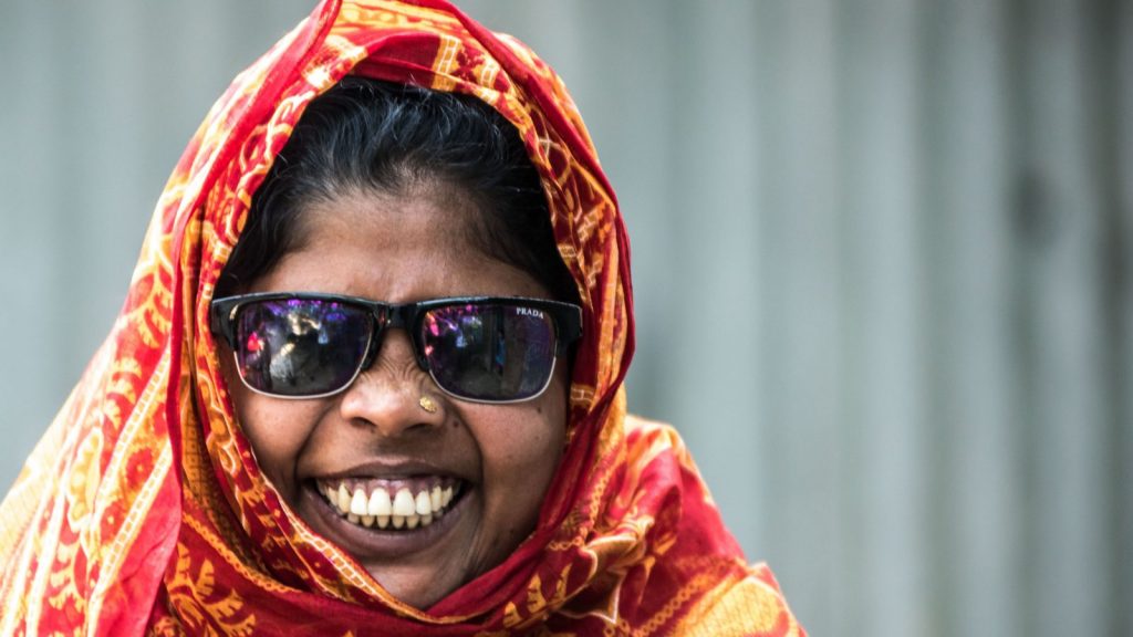 Una donna sorridente indossa occhiali da sole e una sciarpa arancione.