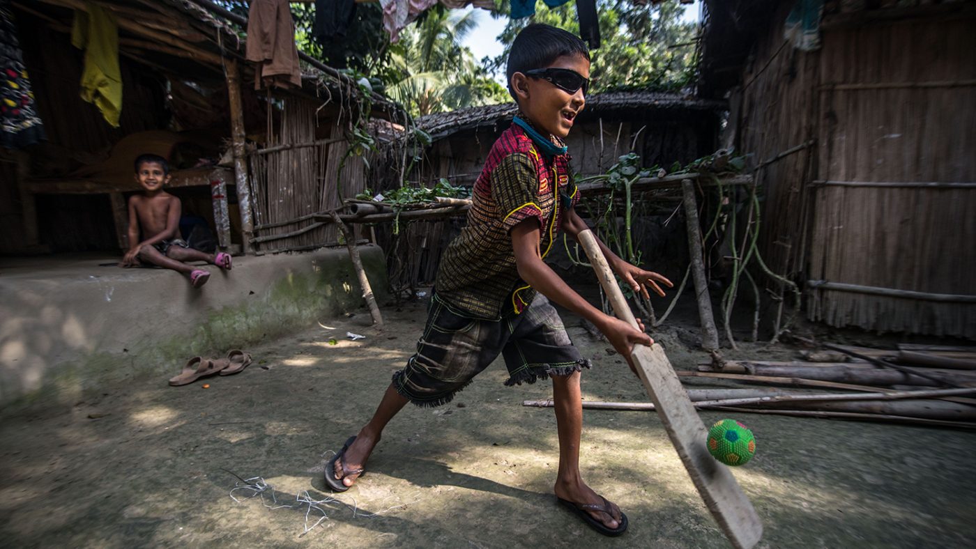 Un bambino con gli occhiali da sole sta giocando a cricket.