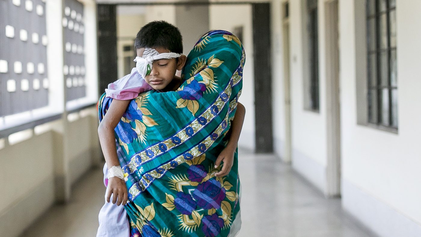Un bambino con la benda sull'occhio è in braccio alla sua mamma in un corridoio dell'ospedale.