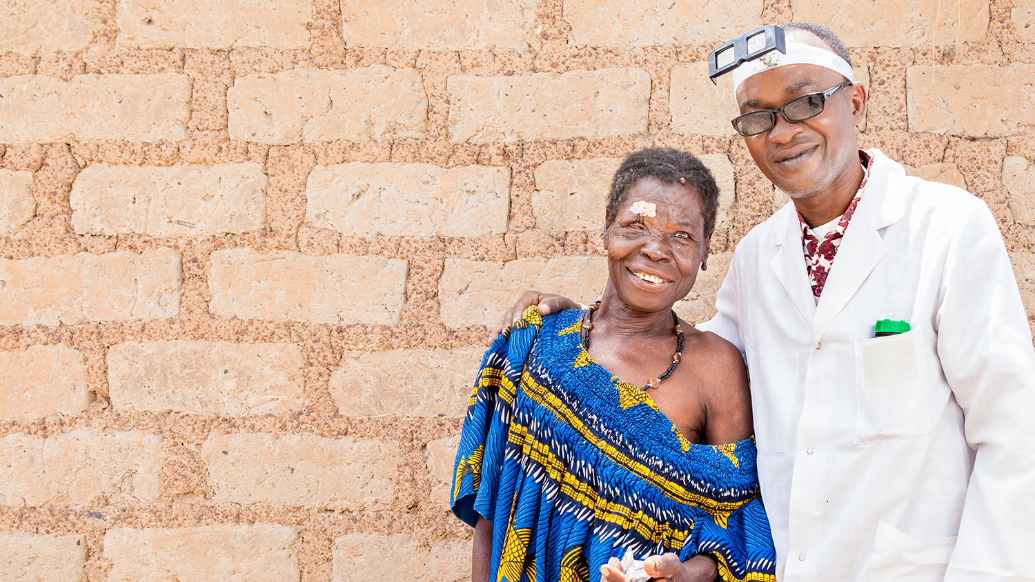 Un dottore sorridente abbraccia una donna appena operata, anche lei sorridente.