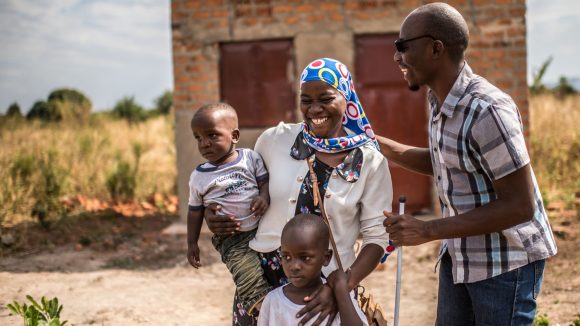 Un uomo cieco con il bastone e gli occhiali e una donna abbracciano i propri figli sorridendo.