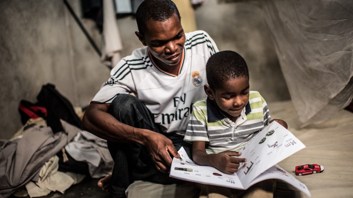 Un bambino è seduto a leggere un libro insieme al suo papà.