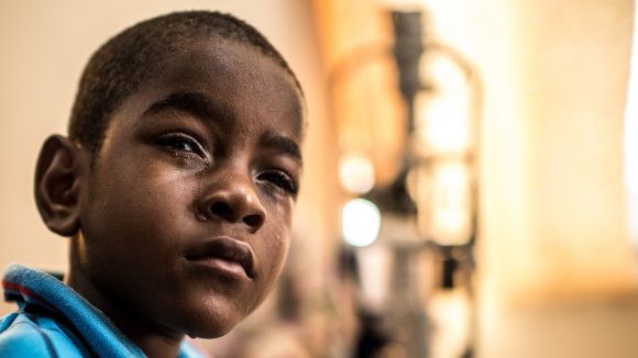 Un bambino triste in primo piano guarda davanti a sè e ha il viso rigato di lacrime.