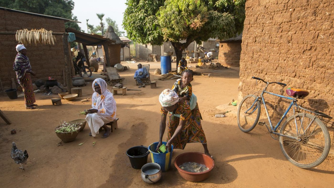 Una donna con una bambina sulla schena è china su un secchio di acqua.