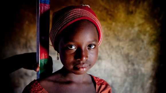 Una bambina vestita di rosso sorride. Alle sue spalle il bastone per la misurazione.