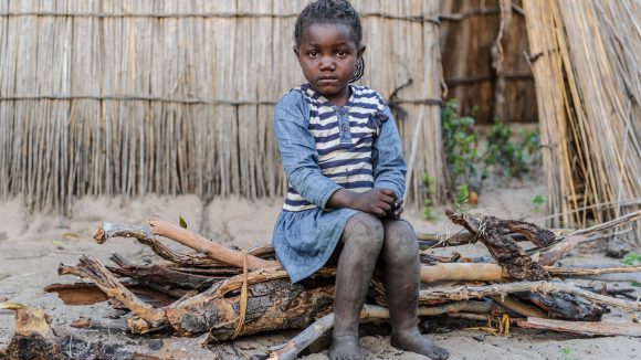 Una bambina seduta sul tronco di un albero guarda di fronte a sè con lo sguardo triste.