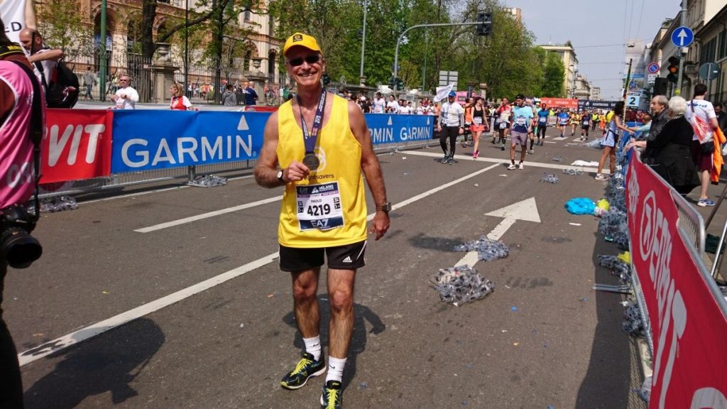 Un maratoneta con la maglietta di Sightsavers sorride e tiene la sua medaglia in mano dopo la corsa