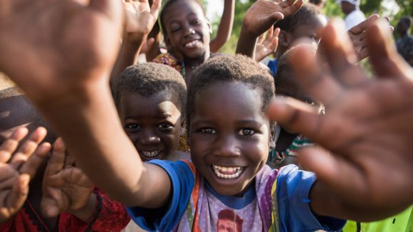 Dei bambini sorridenti in gruppo salutano.