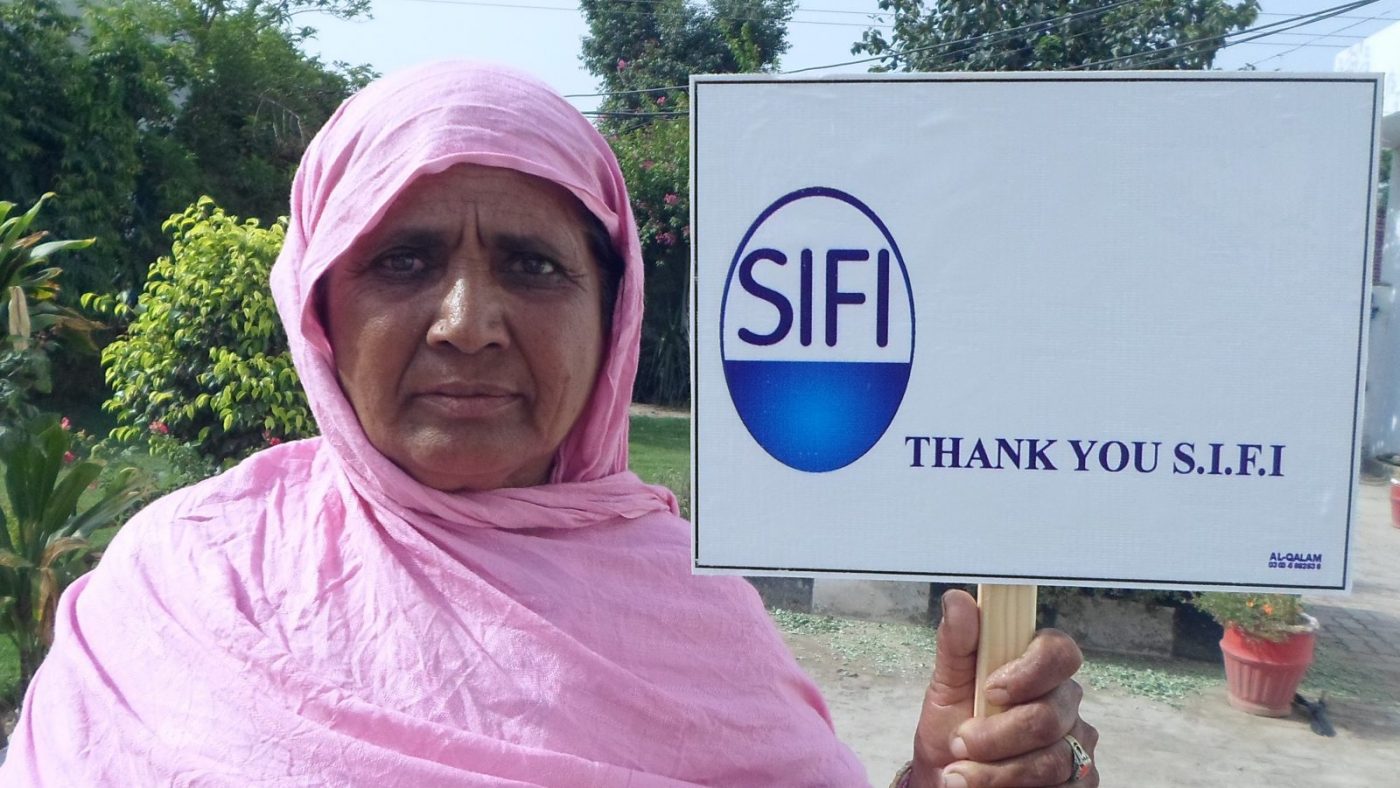 Una donna tiene in mano un cartello con il logo della azienda SIFI che sostiene il lavoro di Sightsavers.