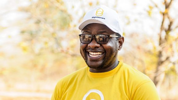 A man smiles, wearing a yellow Sightsavers tshirt.