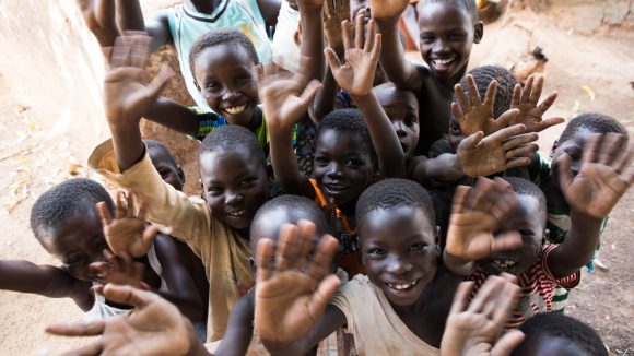 Dei bambini sorridono alla fotocamera e salutano.