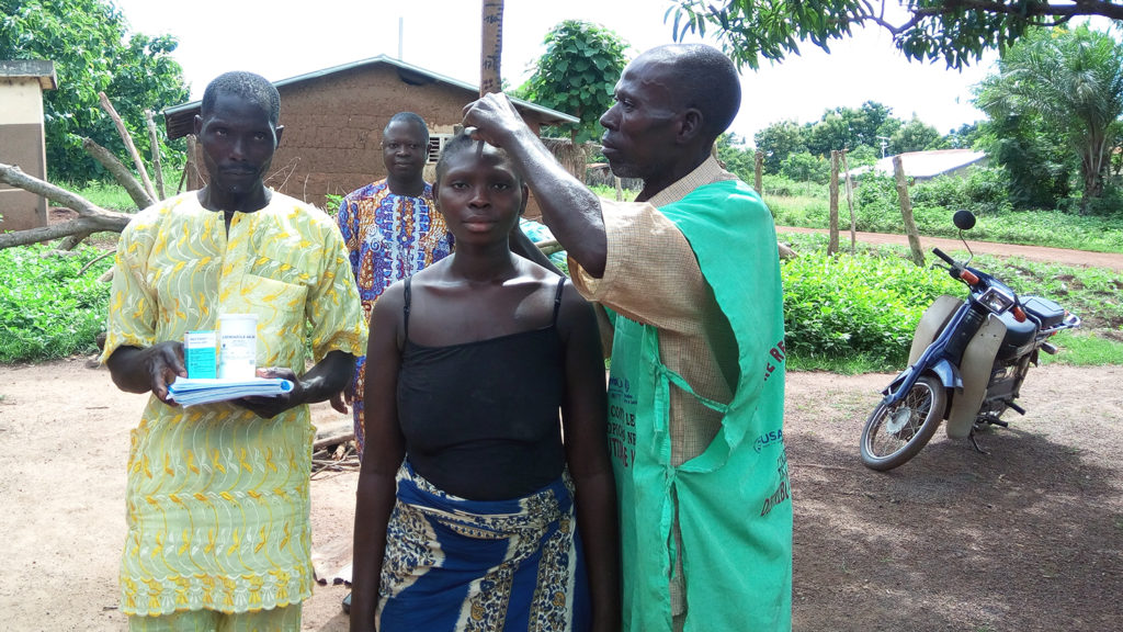 Two men measure the height of a women in order to give her the correct dosage of medicine.