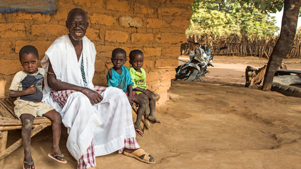 Trachoma patient Aladje sits with his grandchildren outside their home in Guinea-Bissau.