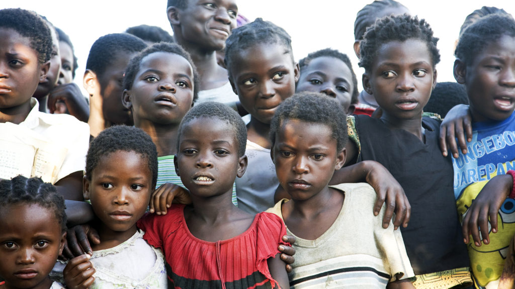 A group of children standing, some have their arms over other children.