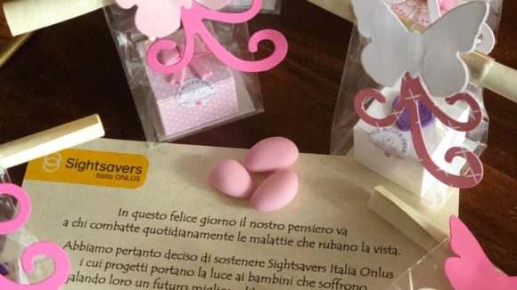 Pergamena di battesimo in mezzo a scatoline porta confetti rosa e bianche a forma di farfalla