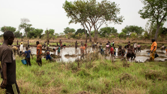 Un folto gruppo di uomini e bambini lavorano nel fiume per sistemare gli argini.