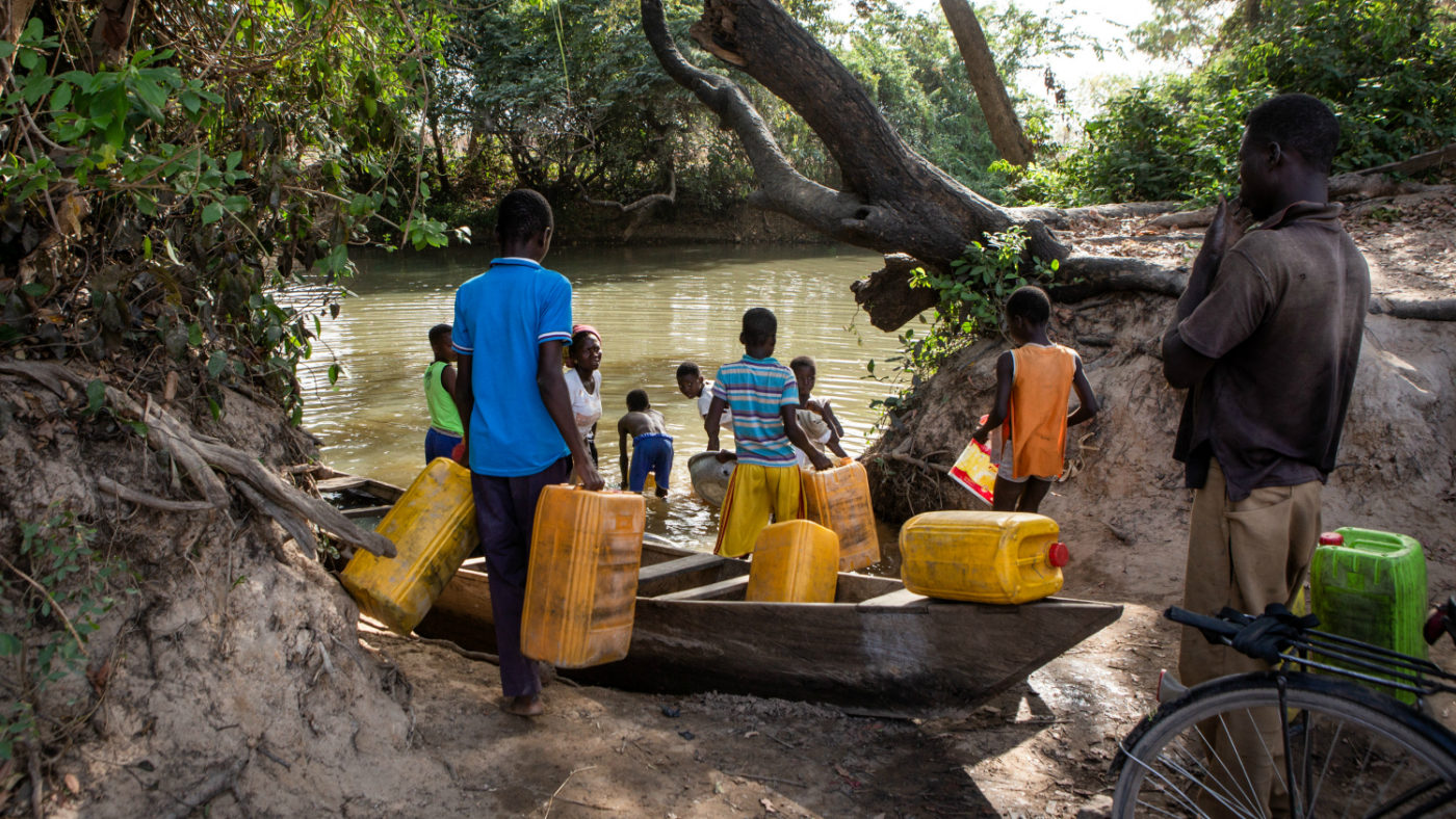Uomini e bambini sulla riva del fiume mentre raccolgono l'acqua con delle teniche di plastica