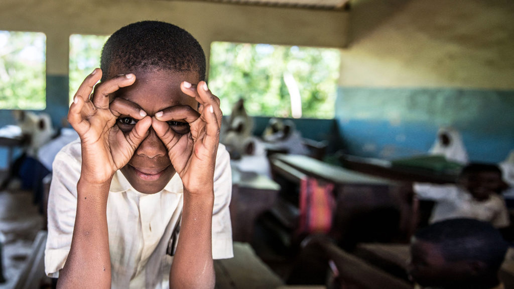 A student in Zanzibar uses his hands to imitate a pair of glasses.