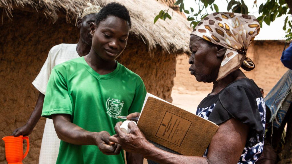 A volunteer health worker called Mary distributes a dose of Mectizan® tablets to a man in a green football shirt.