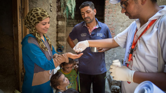 A local health worker hands medication to a woman as another health worker looks on.