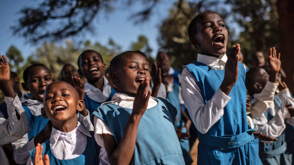School children in Kenya sing songs outside in the sunshine.
