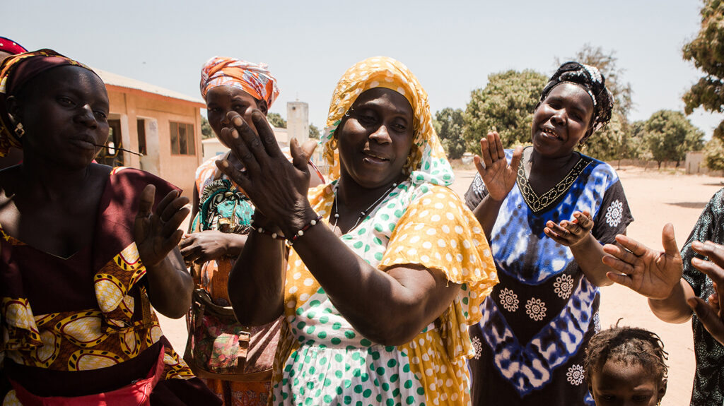 Le donne di un villaggio del Gambia applaudono e sorridono felici.