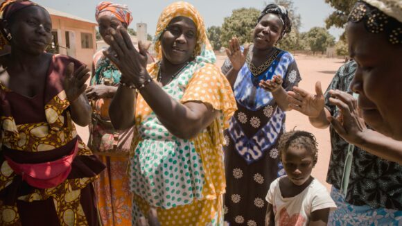 Le donne di un villaggio del Gambia applaudono e sorridono felici.