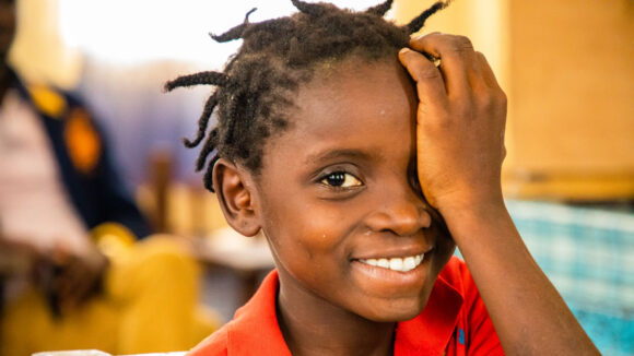 Una bambina sorride mentre si compre l'occhio con la mano.