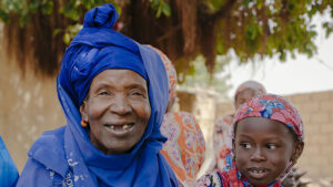 Nar, who had successful treatment for trachoma, sits outside with her two grandchildren. They are all smiling.