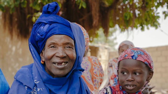 Nar, who had successful treatment for trachoma, sits outside with her two grandchildren. They are all smiling.