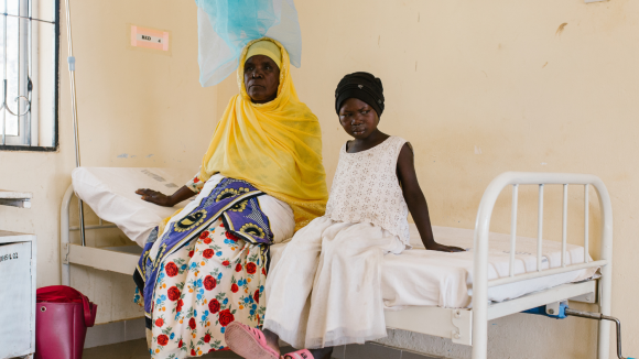Mwamini seduta sul lettino di ospedale con la nonna.