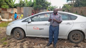 A man reading a leaflet stands next to a white taxi. He is wearing a pair of glasses with black frames.